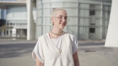 Portrait of woman with shaved hair looking at the camera smiling. Happy young caucasian female standing outdoors. High quality photo
