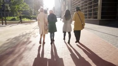 Back view of Four business people, one man and three women, walk and talk outside an office building corporate area. High quality 4k footage