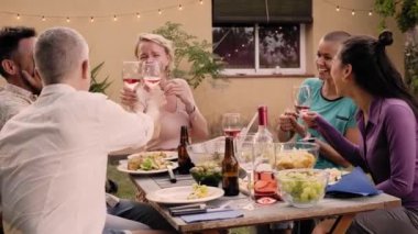 Happy friends having fun outdoors enjoying being together at home garden. Friendship concept of middle aged people toasting with a glass of wine. High quality photo