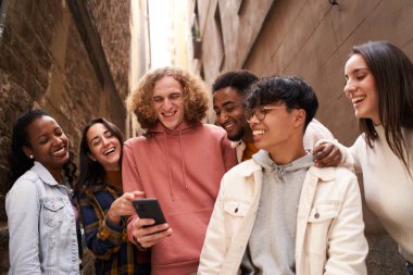 Bir grup mutlu genç açık havada akıllı telefon kullanırken seyyar bir şeyler izleyip gülüyorlar. Teknoloji, arkadaşlık ve toplum kavramı. Yüksek kalite fotoğraf