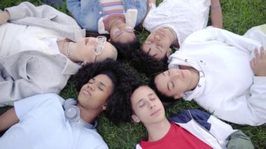 Erkekler ve kızlar çimenlerin üzerinde gözleri kapalı yatıyorlar. Huzurlu ve memnunlar. Üst görünüm portresi. Yüksek kalite fotoğraf