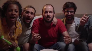 Genç sporseverler bir araya gelip maç izliyorlar. Neşeli arkadaşlar ellerinde içkiler ve patlamış mısır kasesiyle TV 'nin yanında oturuyorlar. Spor ve eğlence anlayışı. Ev arkaplanı.