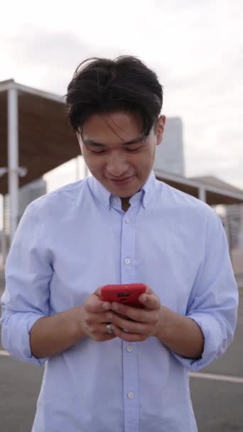 Вертикальное Видео Молодой Веселый Азиат Использует Мобильный Телефон Улице Пишет — стоковое видео