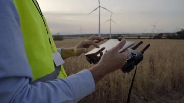 Operatör uzaktan kumanda ve kuadkopter tutuyor. İnsansız hava helikopteri rüzgar alanından başlıyor. Erkek, uzaktan kumandalı bir dron kullanıyor. Drone yenilenebilir enerji kontrolüyle oynayan mühendis