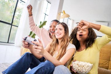 Bir grup genç bayan çok ırklı genç arkadaş evde video oyunları oynuyorlar. Sadece kadınlar oynar ve patlamış mısır yer. - Evet. Yüksek kalite fotoğraf