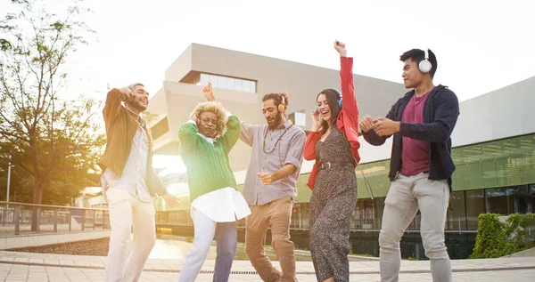 Group of happy people outdoors celebrating and dancing with headphones outdoors. High quality photo