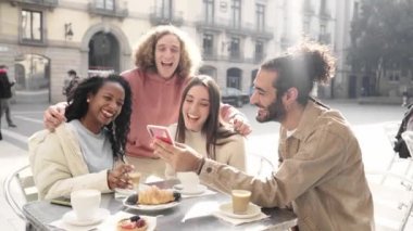 Kafedeki bir grup arkadaş telefonda bir şey izliyor. İnsanlar şehir caddesindeki terasta kahvaltı yapmak için cep telefonu kullanıyorlar. Adam üniversitesini selamlıyor. Yüksek kalite 4k görüntü