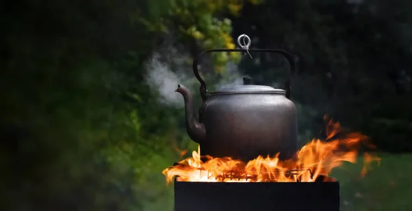 Camping kettle boiling on the grill with steam from the spout on the background of natural nature. widescreen photo