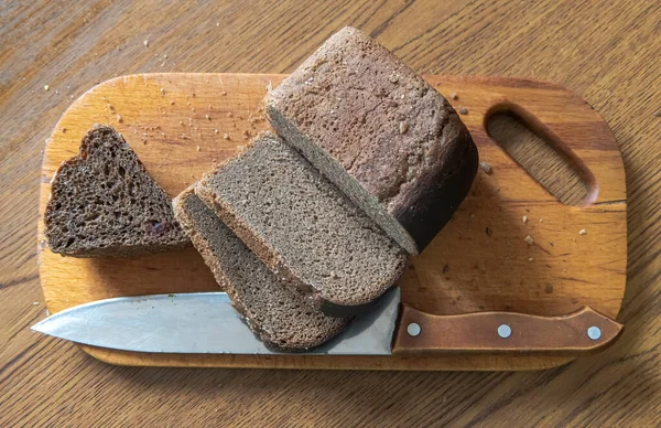 Sliced bread on a wooden board, crumbs around and a knife nearby