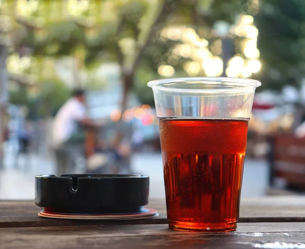 An ashtray and a plastic glass with beer on the background of the bustle of the city