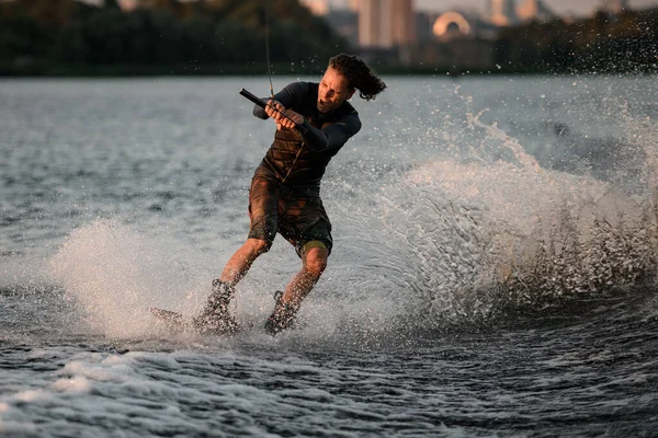 Sportlicher Typ hält Seil in der Hand und rast mit Wakeboard auf dem Fluss. — Stockfoto