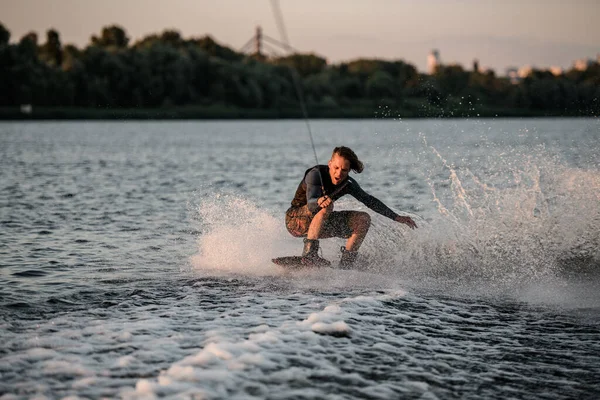 Homme énergique en combinaison de plongée équilibrage sur wakeboard et monter une vague éclaboussante. — Photo