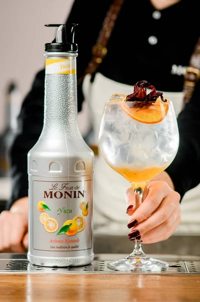 UKRAINE, KYIV - 12 maart 2021: fles Monin yuzu puree en wijnglas van koude zoete cocktail gegarneerd met sinaasappelschijfje — Stockfoto