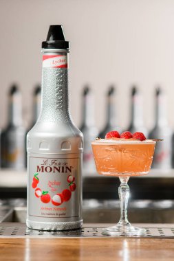 UKRAINE, KYIV - 12 Mart 2021: Monin tarafından hazırlanmış bir şişe liçi şurubu ve ahubu ile süslenmiş kristal şarap kadehi