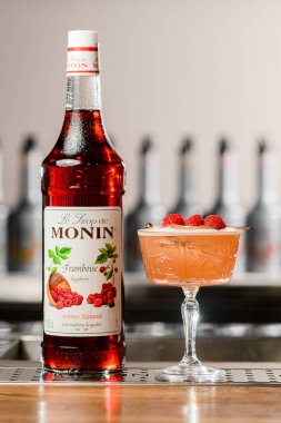 UKRAINE, KYIV - 12 Mart 2021: Monin tarafından hazırlanmış bir şişe ahududu şurubu ve ahubu ile süslenmiş kristal şarap kadehi