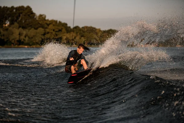 Fuerte atlético wakeboarder macho sostiene la cuerda y enérgicamente montar wakeboard en salpicaduras de agua del río. —  Fotos de Stock