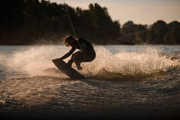 Énergie sportive wakeboarder s'amuser et faire des tours à cheval sur la carte à éclabousser vague de rivière. — Photo