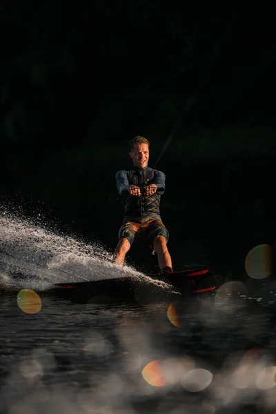 Atletický muž wakeboarder sebevědomě jezdí na desce na stříkající řece vlny. — Stock fotografie