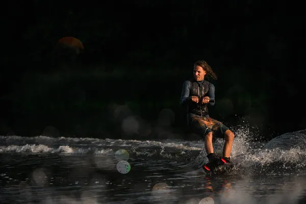 Uomo bagnato in muta energicamente in equilibrio sulla superficie dell'acqua sul wakeboard — Foto Stock
