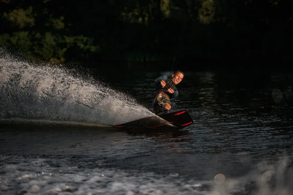 Forte atletico uomo in muta abilmente in equilibrio sulla superficie dell'acqua sul wakeboard — Foto Stock