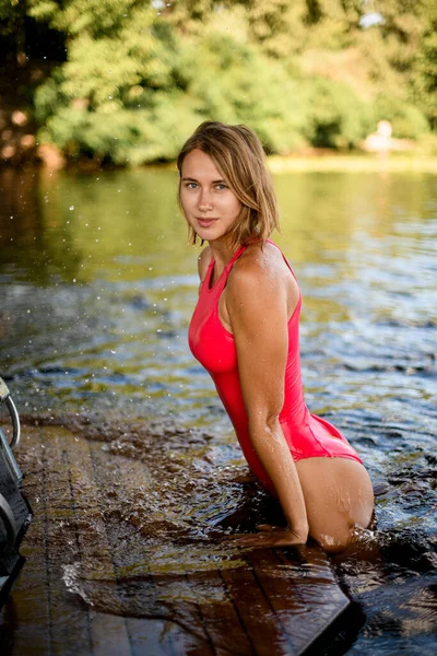 Mulher atraente em maiô posando esticando-se para fora da água e inclinando as mãos na borda do barco — Fotografia de Stock