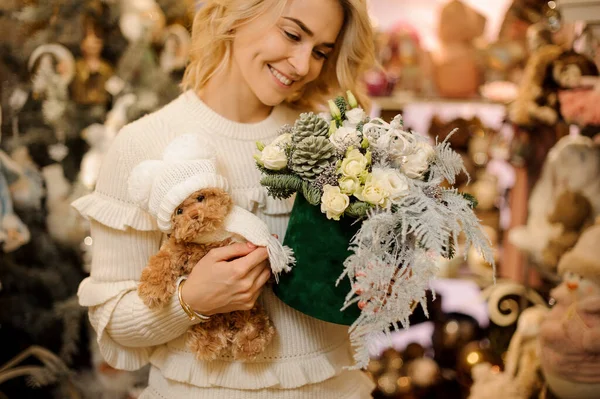 beautiful floral arrangement and teddy bear in the hands of smiling blonde woman.