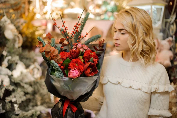 Ramo de flores rojas decoradas con ramas de abeto y eucalipto en las manos de la mujer — Foto de Stock