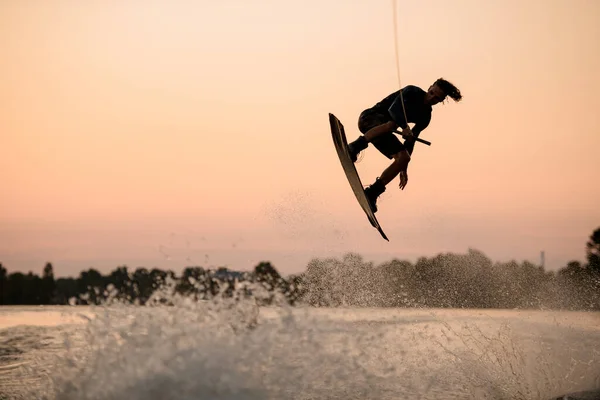 Homme actif sautant par-dessus les éclaboussures vague sur wakeboard tenant à la corde. Activités nautiques. — Photo