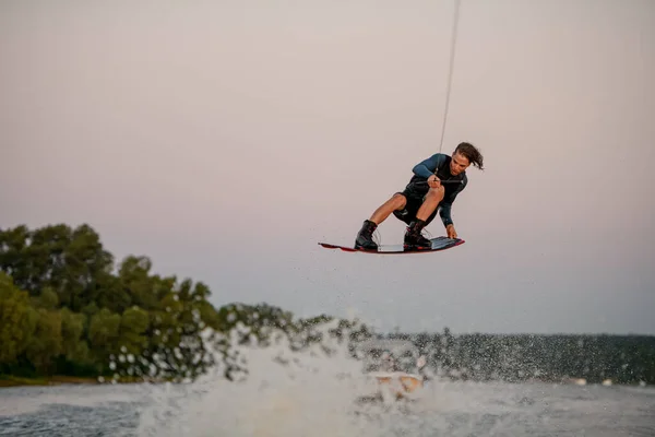 Hombre de energía volando sobre la ola salpicando en wakeboard aferrándose a la cuerda —  Fotos de Stock