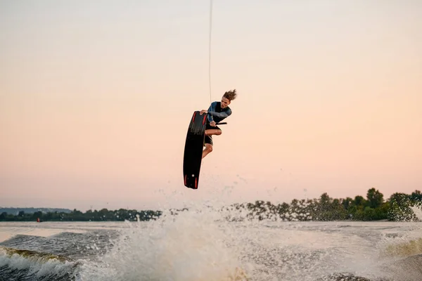 Pria energi terlibat dalam olahraga air dan melompat di gelombang percikan pada papan bangun — Stok Foto
