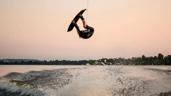 Laki-laki wakeboarder dengan hebat melompat dan membalik pada papan bangun di atas gelombang percikan — Stok Foto