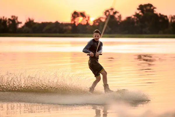 Homme actif wakesurfer équitation éclaboussures vague sur fond de coucher de soleil lumineux — Photo