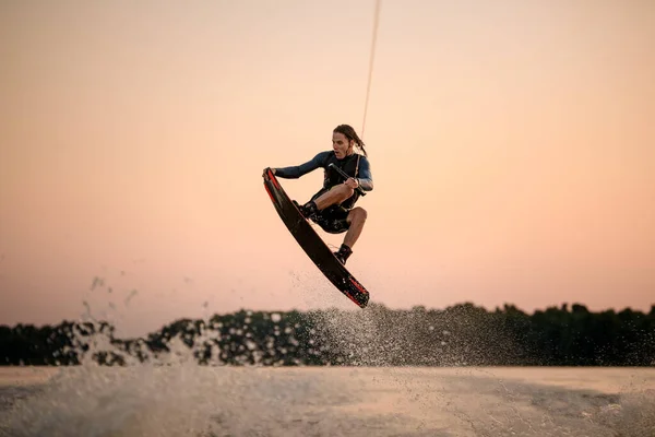 Активный сильный человек делает трюк во время прыжка с вейкбордом на фоне неба. — стоковое фото