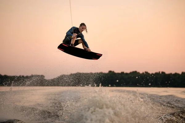 Sportsman making trick in jump time with wakeboard on sky background. — Stock Photo, Image