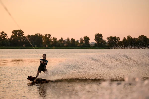 Vista de alegre wakesurfer macho cabalgando agua y un montón de salpicaduras detrás de él —  Fotos de Stock