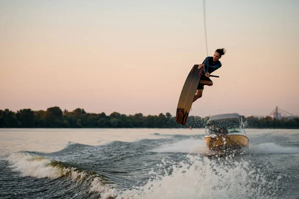 El hombre atlético se divierte y salta en la ola salpicando en un wakeboard —  Fotos de Stock