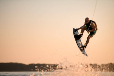 Enerji kaslı sporcu atlama zamanında gökyüzünün arka planına karşı wakeboard ile hile yapıyor