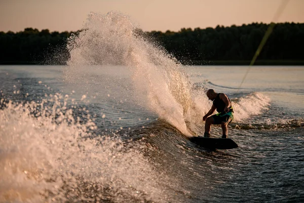 Uomo attivo cavalca energicamente giù su onda splasing su wakesboard. — Foto Stock