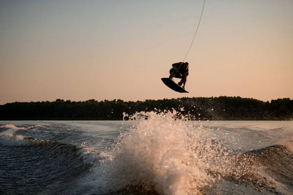 Wspaniały widok muskularny człowiek skacze wysoko z wakeboard nad chlapanie wody na tle nieba — Zdjęcie stockowe