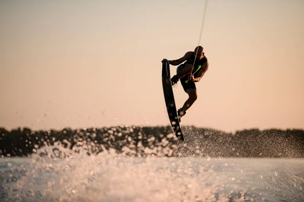 Kaslı adam atlama zamanında gökyüzünün arka planına karşı wakeboard ile numara yapıyor. — Stok fotoğraf