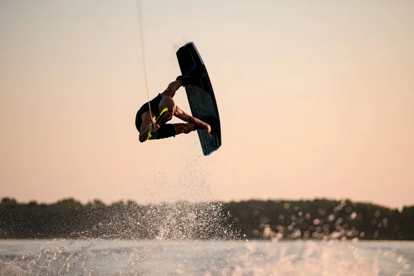 great view of muscular man making trick in jump time with wakeboard against the backdrop of the sky