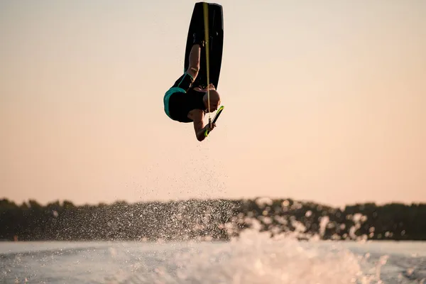 Vacker utsikt över atletisk man gör flip trick i luften på wakeboard mot solnedgången himlen — Stockfoto