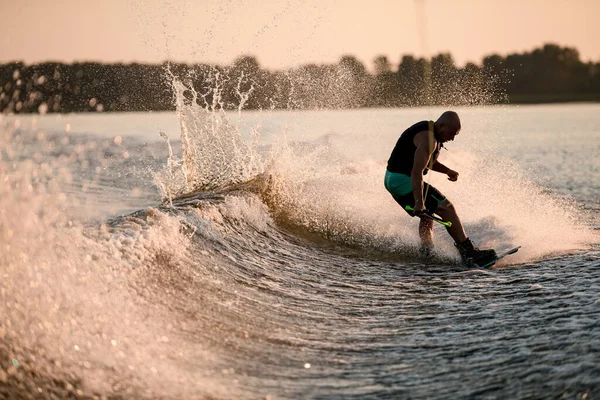 Atletisk kille håller rep och ridning wakeboard på stänk flod våg. — Stockfoto