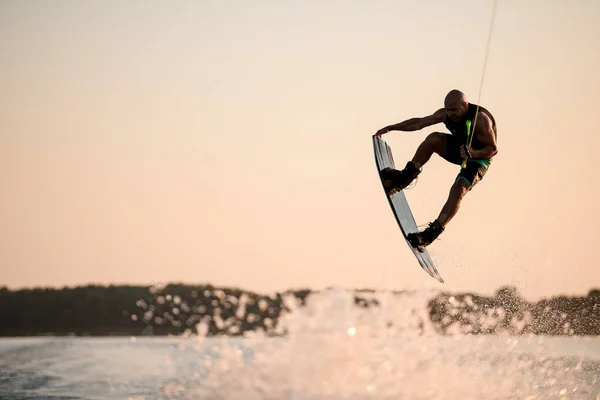 Enerji kaslı adam atlama zamanında gökyüzünün arka planına karşı wakeboard ile hile yapıyor. — Stok fotoğraf