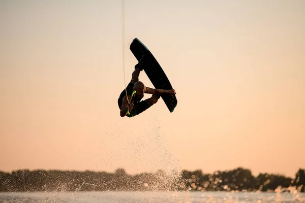 Superbe vue de l'homme sautant magistralement et flips avec wakeboard sur fond de ciel couchant — Photo