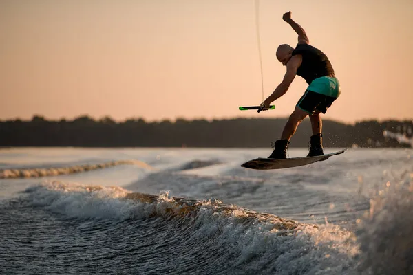 Ottima vista dell'uomo muscoloso che tiene la corda e salta con il wakeboard sopra spruzzi d'acqua — Foto Stock