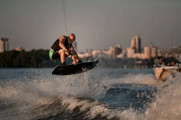 Energia muscolare uomo abilmente saltando alto sopra spruzzi d'onda sul wakeboard — Foto Stock