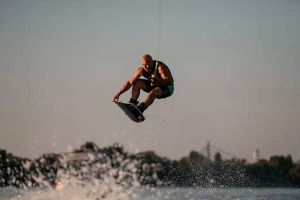 Atletisk stark muskulös man skickligt hoppa högt över stänk våg på wakeboard — Stockfoto