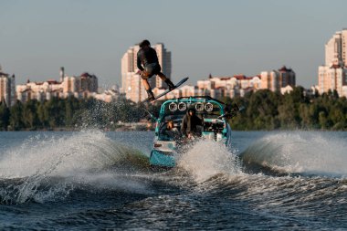 Wakeboard 'cu kayığın arkasında hızlı hareket ediyor. Halat tutuyor ve su sıçratan bir nehir dalgasında zıplıyor..