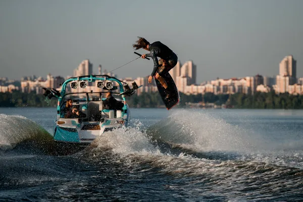 Énergie wakeboarder se déplaçant rapidement derrière le bateau tenant la corde et sautant magistralement haut sur les éclaboussures vague de rivière. — Photo